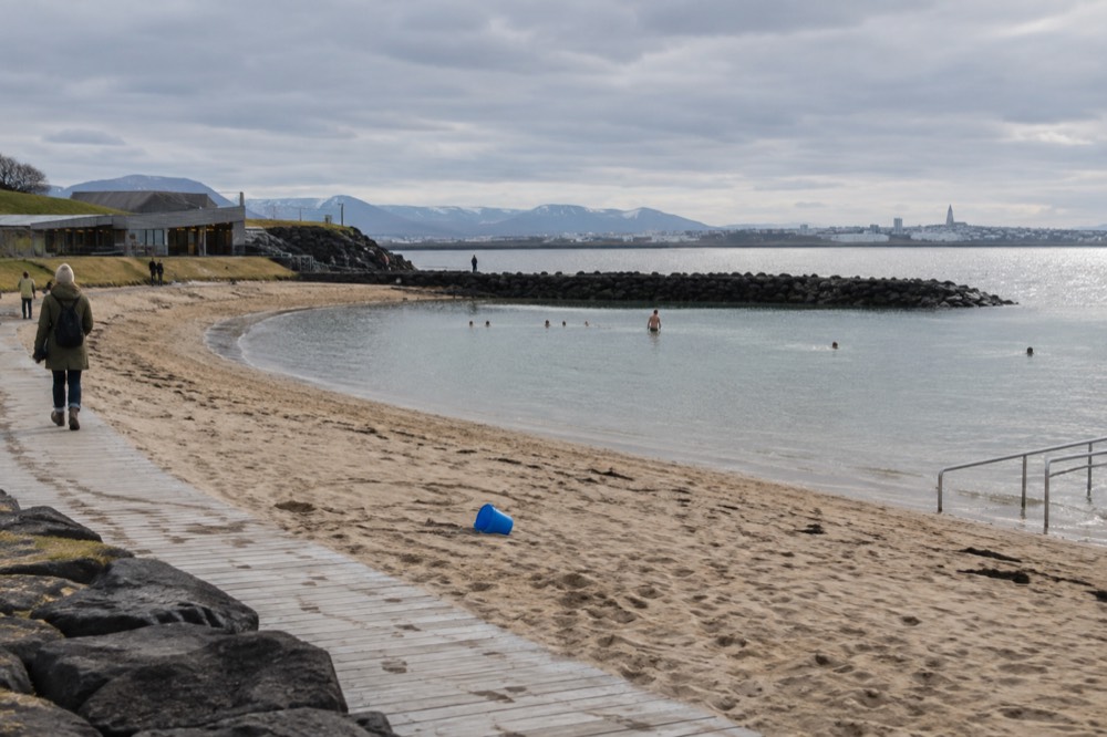 A sheltered sandy cove with calm water and a wooden walkway under an overcast sky