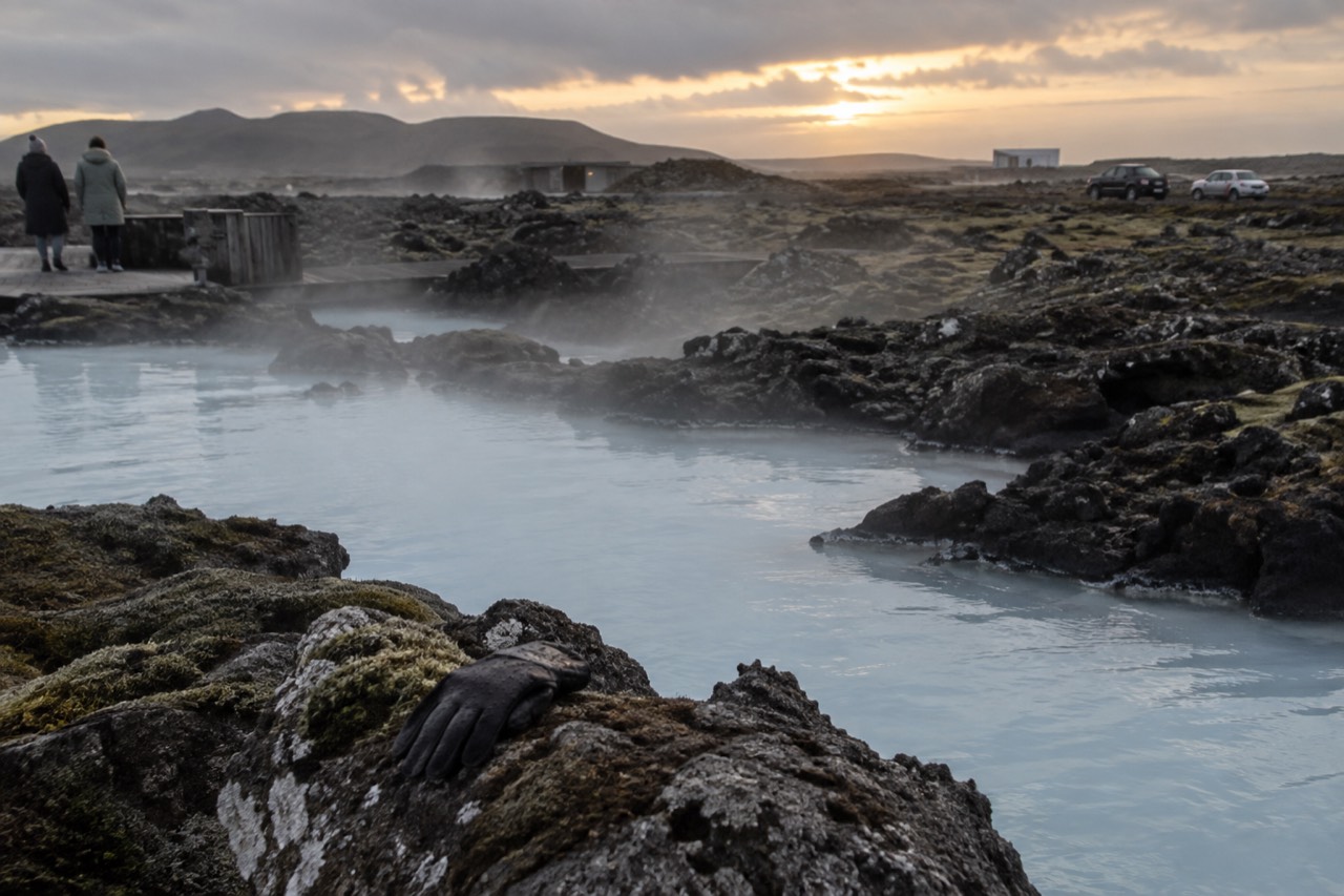 Steam rising from pale blue geothermal water against a dark volcanic rock landscape