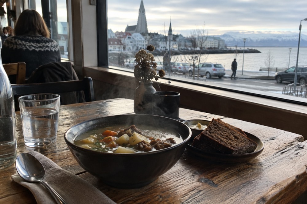 A bowl of lamb soup and bread on a wooden cafe table