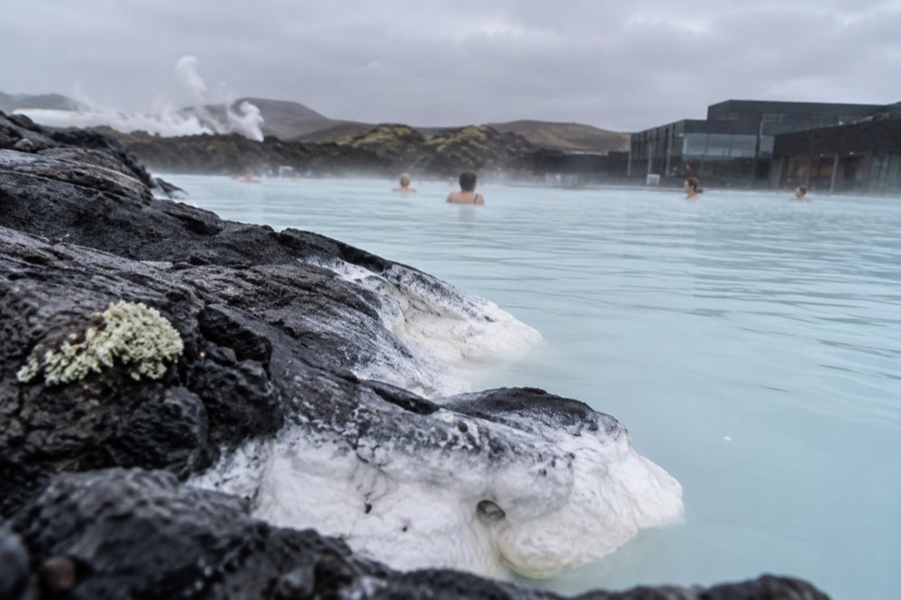 A close view of the Blue Lagoon's white silica mud smeared on a rock edge, with the blue water and steam behind it, no people visible.