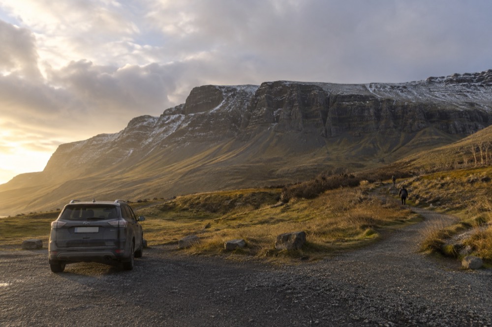 A gravel trailhead car park beneath a rocky Icelandic hillside