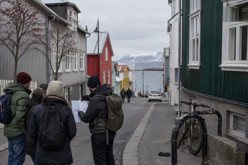 A group of tourists gathered around a guide holding a map near the coloured houses of central Reykjavik