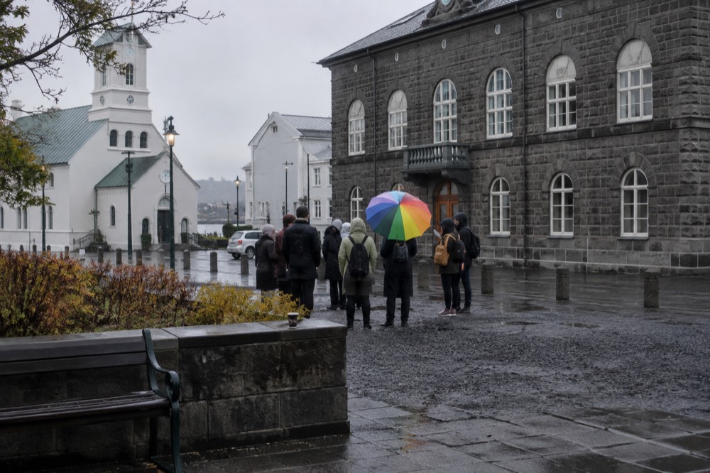 A guide with a rainbow umbrella addressing a small group in a city square