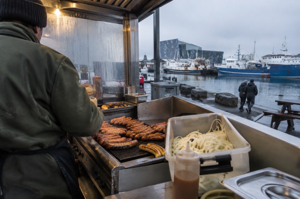 A hot dog stand beside the Reykjavik harbor with a grill full of sausages
