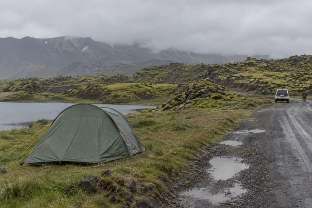A small tent beside a gravel road with moss covered hills behind it