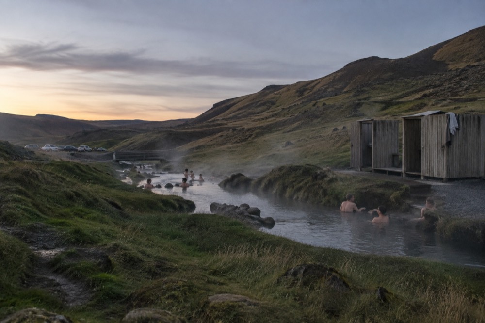 People bathing in a warm geothermal river surrounded by mossy hills