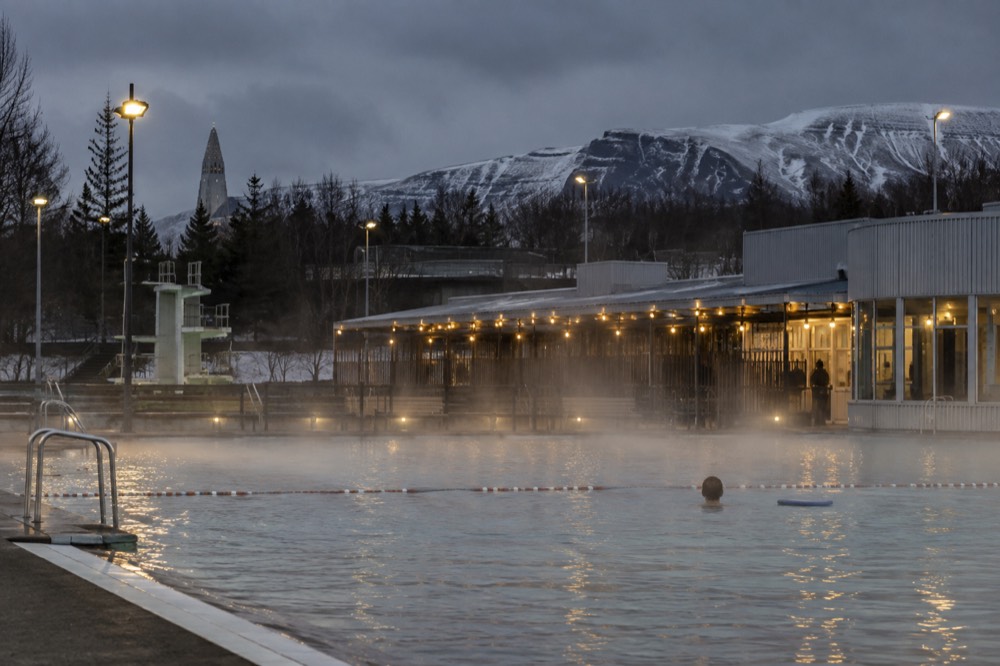 An outdoor geothermal pool steaming under a dark winter sky with string lights