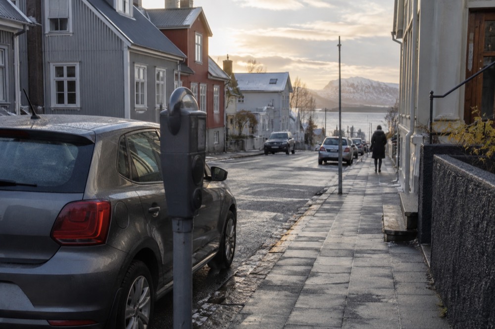 Parking payment meter on a Reykjavik sidewalk beside a parked car