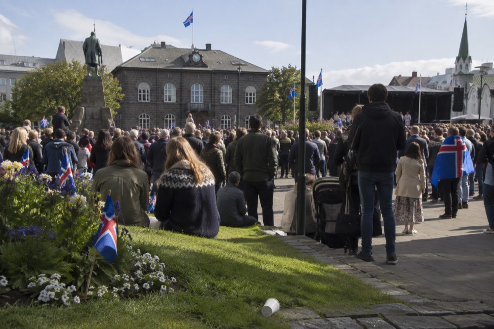 Crowds gathered in a green Reykjavik park on a festive day with flags and a stage area