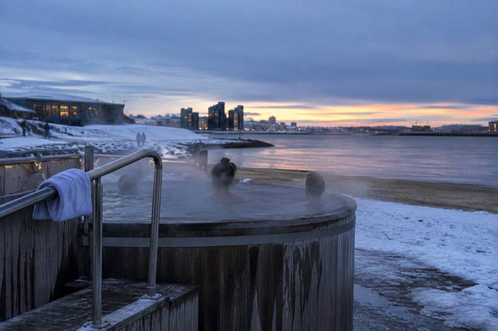 A steaming geothermal beach with a wooden hot tub under a winter sky