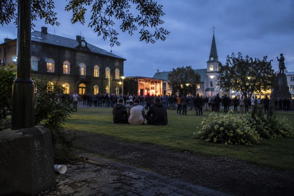 Crowds in a city square at dusk with stage lights