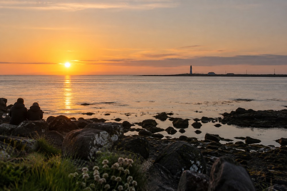 Low golden sunlight over a flat sea with a distant lighthouse on the horizon