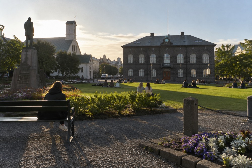 Austurvöllur square in summer with people sitting on the grass and the Parliament building in the background