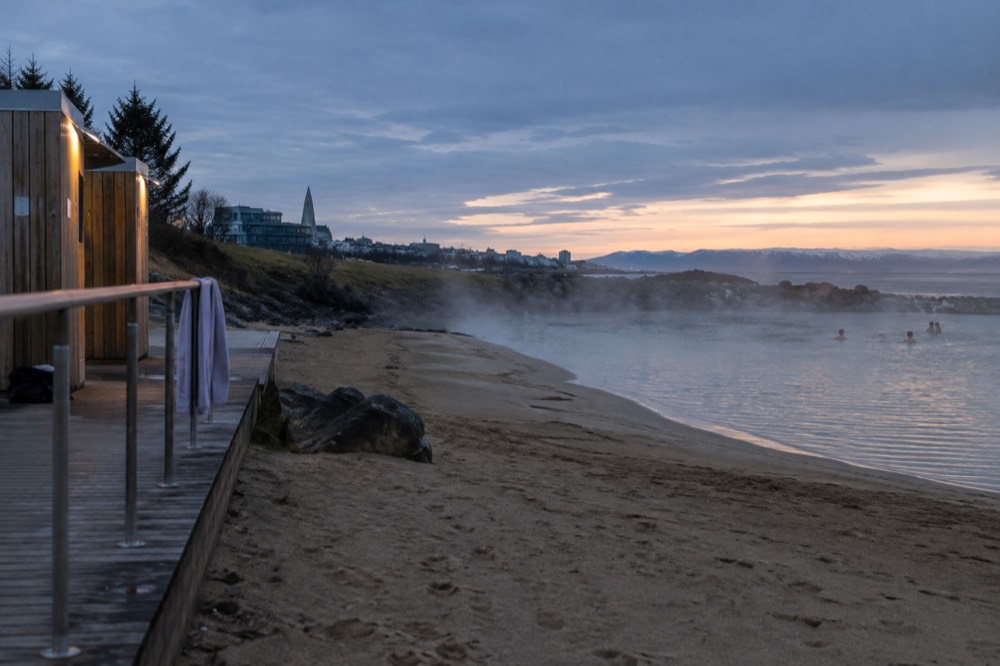 Geothermal lagoon edge with a sandy beach and changing huts
