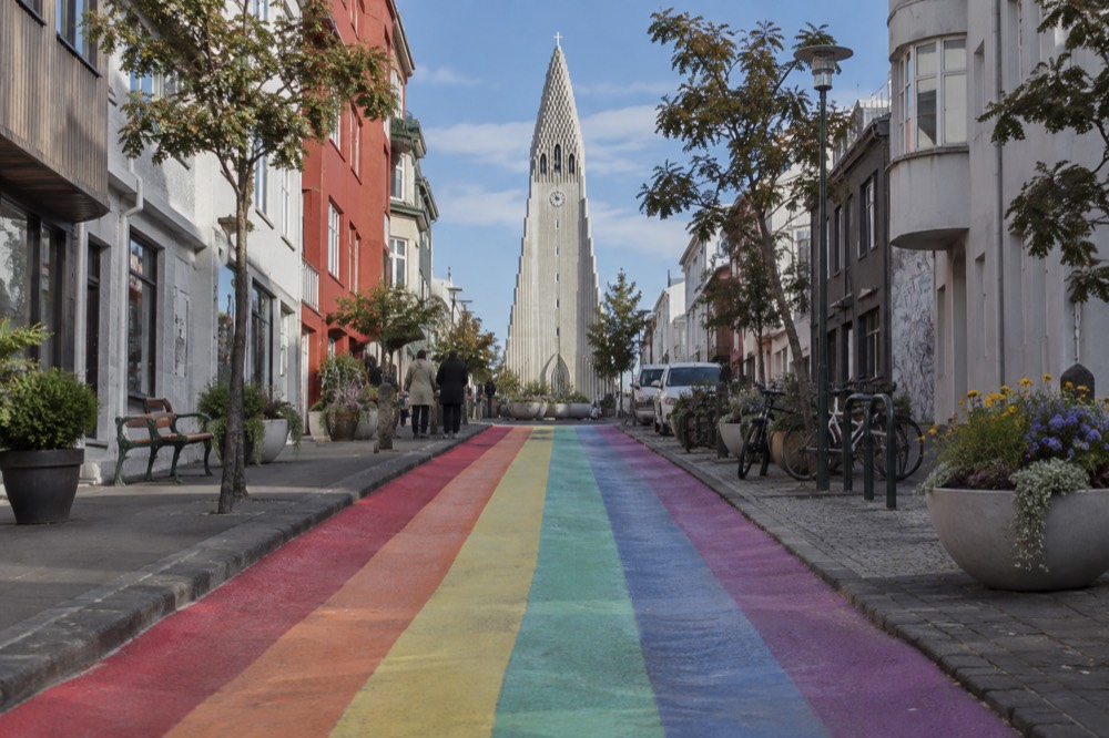 A rainbow-striped pedestrian street rising toward a large stone church tower