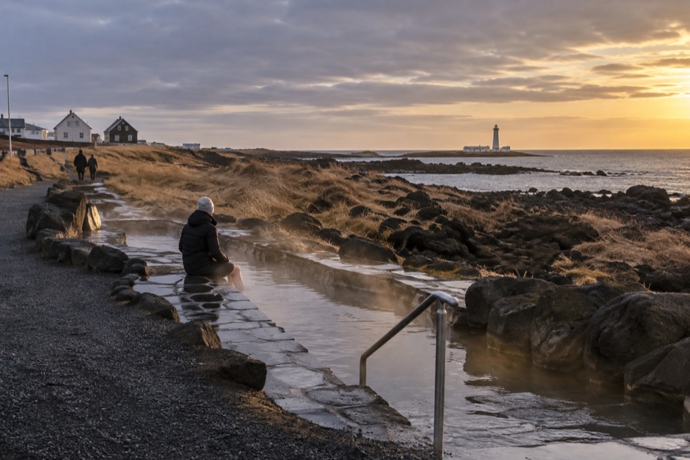 Stone foot bath channel beside a gravel coastal path with sea and distant lighthouse