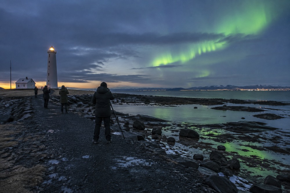 People in winter clothing standing on a dark path watching green light over the water