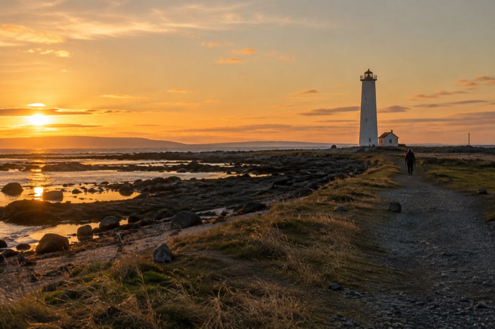 A small lighthouse on a rocky peninsula under a wide evening sky