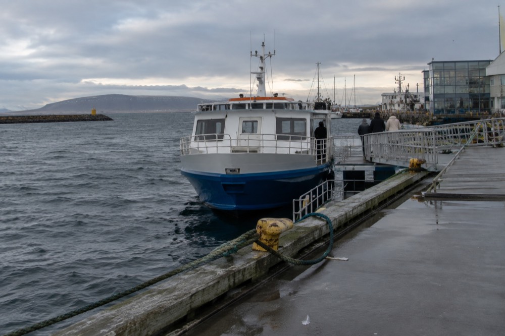 A small ferry boat at the harbour pier with a low island on the horizon