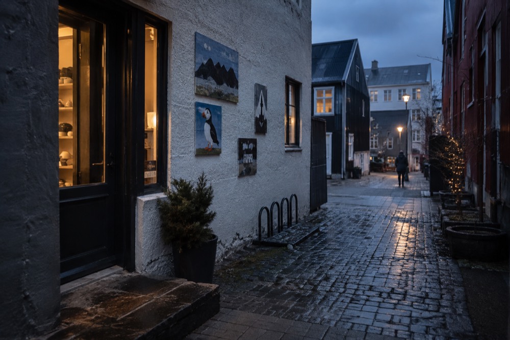 A narrow alley in Reykjavik with small painted artworks on the walls beside a shop doorway