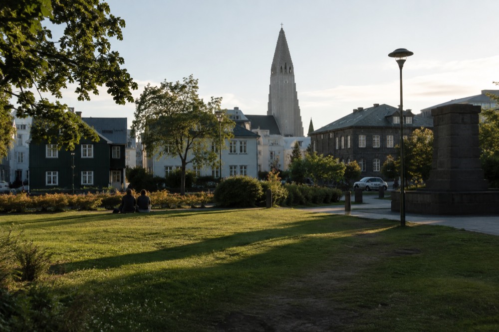 A city square with a church spire in the background and colorful low buildings along a street