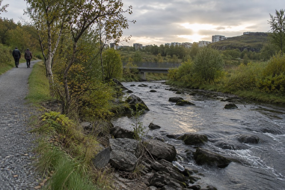 A gravel path beside a shallow river through a green valley