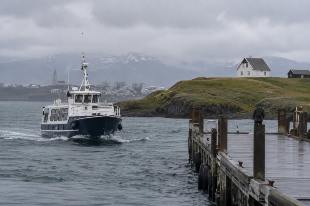 A small passenger ferry approaching a wooden jetty beside a grassy island shore